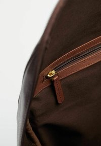 Ruskean kankaan sisäosa, jossa on vetoketjullinen tasku. Vetoketjassa on kultaiset yksityiskohdat ja nahkavetotanko. Näkyvissä on myös teksturoitu vuori.