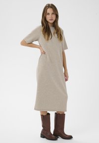 Gai bēšs midi kleita ar īsām piedurknēm, sānu kabatām un brīvu piegriezumu, apvienota ar brūnām līdz ceļiem augstām zābakiem. Gluda auduma tekstūra.