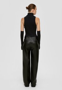 Schwarzer, gerippter Rollkragenpullover, kombiniert mit hochgeschnittenen, weiten schwarze Kunstlederhosen, die über Gesäßtaschen und eine glatte Textur verfügen.