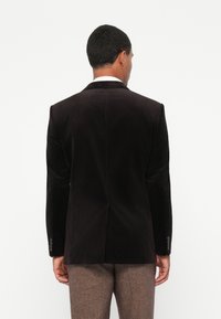 Casaco de veludo cotelê preto com colarinho tipo notch e duas aberturas nas costas. Apresenta punhos com botão e uma textura suave e macia.