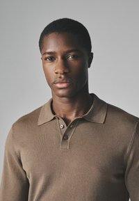 Braunes Poloshirt aus Strickstoff mit kurzen Ärmeln, einem flachen Kragen und einer Knopfleiste mit zwei Knöpfen. Glatte Textur und schmale Passform.