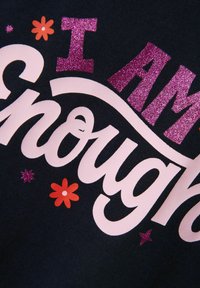 Telas negras con un texto impreso audaz: "SOY" en rosa brillante, "Suficiente" en blanco, con pequeñas flores de colores y estrellas como acentos.