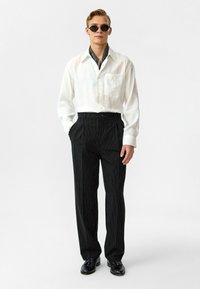 Witte blouse met kraag en zak, zwart gestreepte broek, zwarte zonnebril en zwarte schoenen. Geweven stof met een relaxte fit.