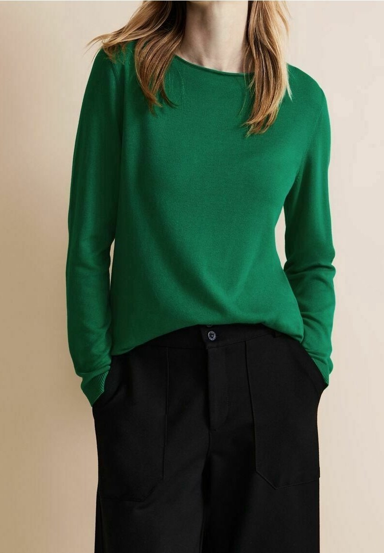 Grüner Pullover mit langen Ärmeln aus weichem Strickmaterial und runder Ausschnitt, kombiniert mit hoch taillierten schwarzen Hosen mit Fronttaschen.