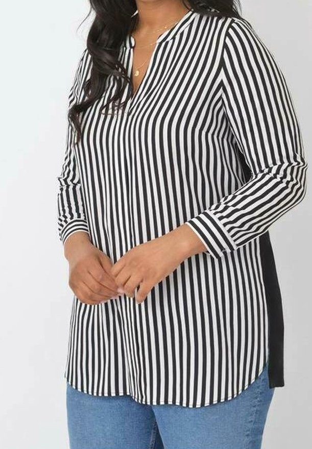 Blusa a righe bianco e nero con scollatura a V, maniche lunghe e spacchetti laterali. Il tessuto ha una texture liscia, abbinata a jeans in denim blu.