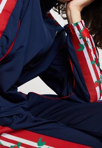 Marinträningsdräkt med röda randiga detaljer och broderade rosor på ärmarna. Elastiska mudd och slät tygtextur.