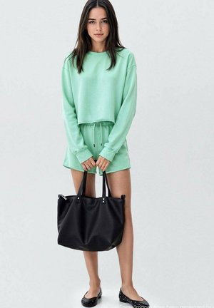 Sweatshirt court vert menthe et shorts assortis en tissu doux, accompagnés d'un grand sac fourre-tout noir avec des poignées doubles et des accents en argent.