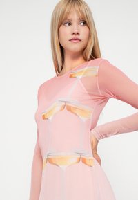 Ilga rankovė rožinė grežinėlių suknelė su spausdintu šampano taurių dizainu, su prigludusia siluetu ir permatomu tekstūru.