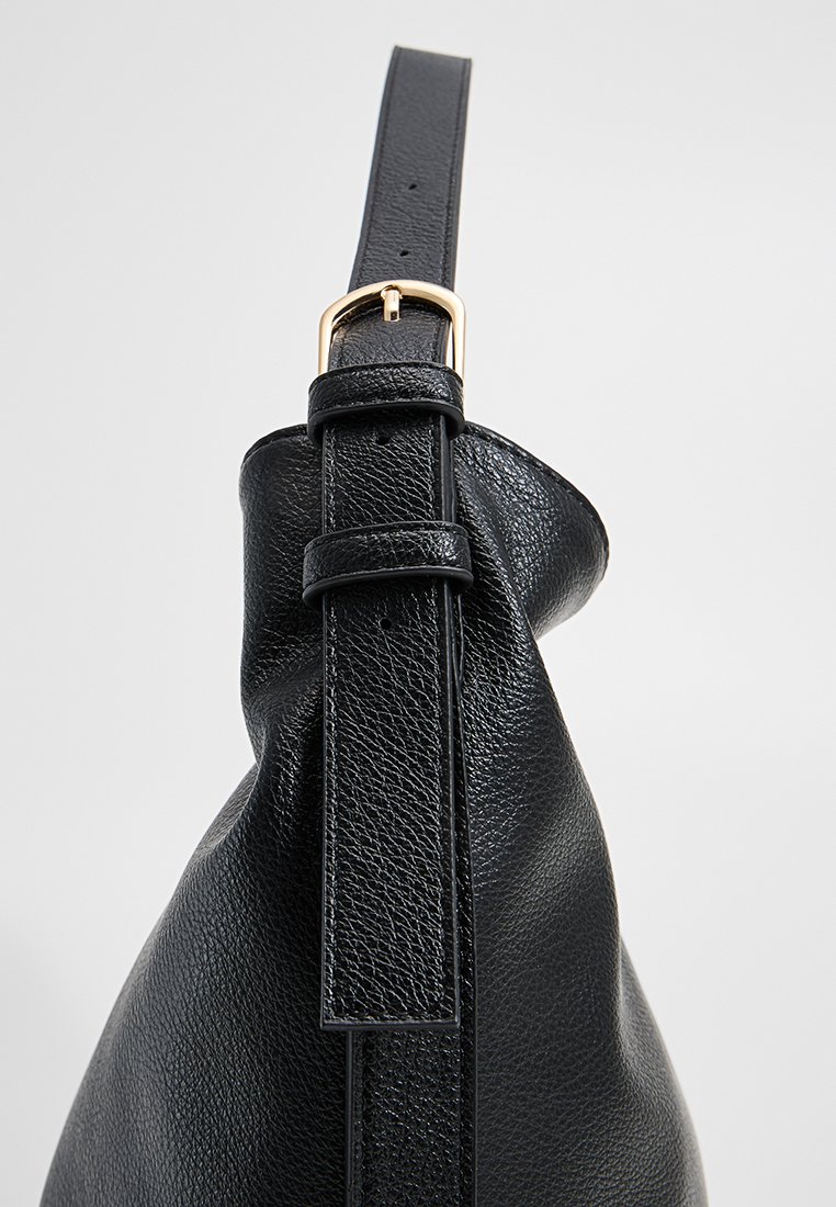 Sac en cuir noir avec une texture, doté d'une bandoulière plate avec une boucle en or et d'une forme décontractée, conçu pour un usage quotidien.