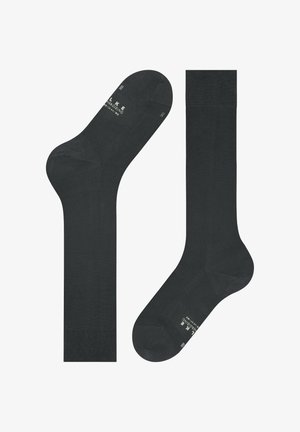 Due calzini neri al ginocchio stesi, uno mostra la parte superiore con il bordo a maglia, l'altro presenta la suola con testo bianco e indicazioni della misura.