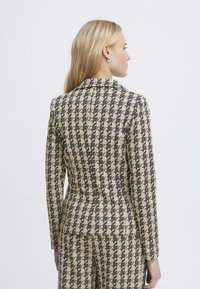 Beige a černý tvídový blejzr s houndstooth vzorem, přiléhavý střih s klopovým límcem a upravenými švy, zobrazený zezadu.