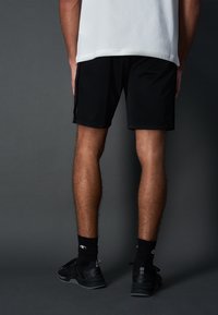 Shorts sportivi neri con una texture liscia, lunghezza fino al ginocchio, abbinati a calzini neri e scarpe da allenamento. Presentano un design semplice e nessun logo visibile.
