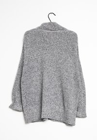 Cardigan gris en tricot avec un motif texturé, à l'avant ouvert et à manches retroussées, suspendu à un cintre noir sur fond blanc.