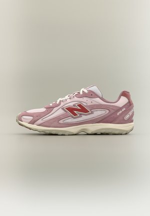 Chaussure de sport rose clair et blanche avec un logo "N" rouge, une semelle beige et "204L" imprimé sur le talon, vue de profil sur un fond neutre.