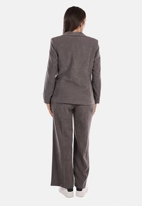 Blazer in suede grigia e pantaloni a gamba larga, caratterizzati da una texture liscia e una vestibilità su misura. Indossati con sneaker bianche, visti da dietro.