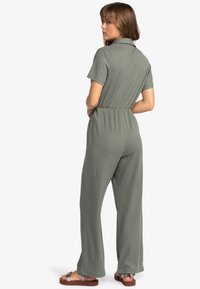 Olijfgroene jumpsuit met korte mouwen, een kraagachtige halslijn, elastische tailleband en een wijde broekspijpen ontwerp, gemaakt van een gestructureerd, rekbaar materiaal.
