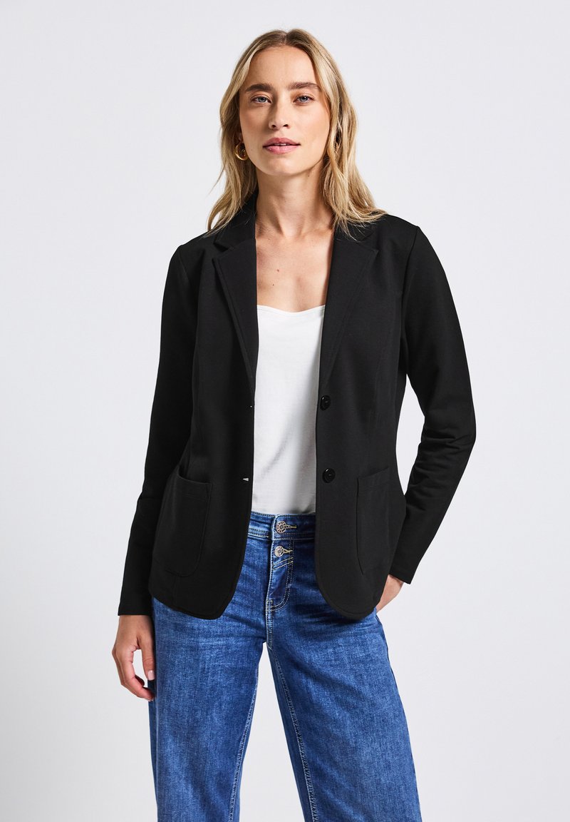 Černý blazer s přizpůsobeným designem, dvěma předními kapsami a dvěma knoflíky. Hladká látka a strukturovaný silueta v kombinaci s lehkými džíny.