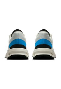 Hvide og blå sneakers med en struktureret overdel, en sort hæl-accent og en tyk hvid sål. Har en afrundet form og minimal detaljering.