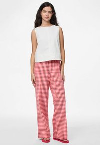 Top bianco senza maniche con scollo rotondo, abbinato a pantaloni rosa a quadrati a gamba larga. Taglio rilassato, tessuto leggero e sandali bassi.