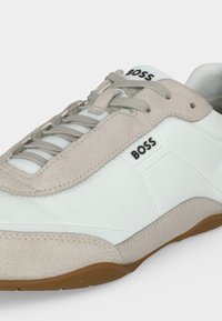 Baskets en cuir blanc et beige avec des accents en daim, lacets beiges, semelle marron et logo « BOSS » sur la languette et le côté.