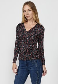 Schwarzes Langarmoberteil mit tiefem V-Ausschnitt, das ein florales Muster in Rot, Weiß und Grün aufweist. Raffinierte Details an der Taille.
