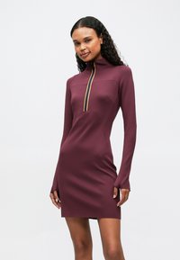 Bordová priliehavá šaty s dlhými rukávmi, vysokým golierom a polovičným zipsom vpredu, ktorý má žlté a modré lemovanie. Hladká, pružná tkanina.