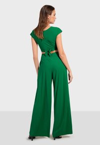 Zeleni dvodijelni outfit s kratkim rukavima i vezanjem na leđima, u kombinaciji s hlačama širokih nogavica. Glatka, rastezljiva tkanina.