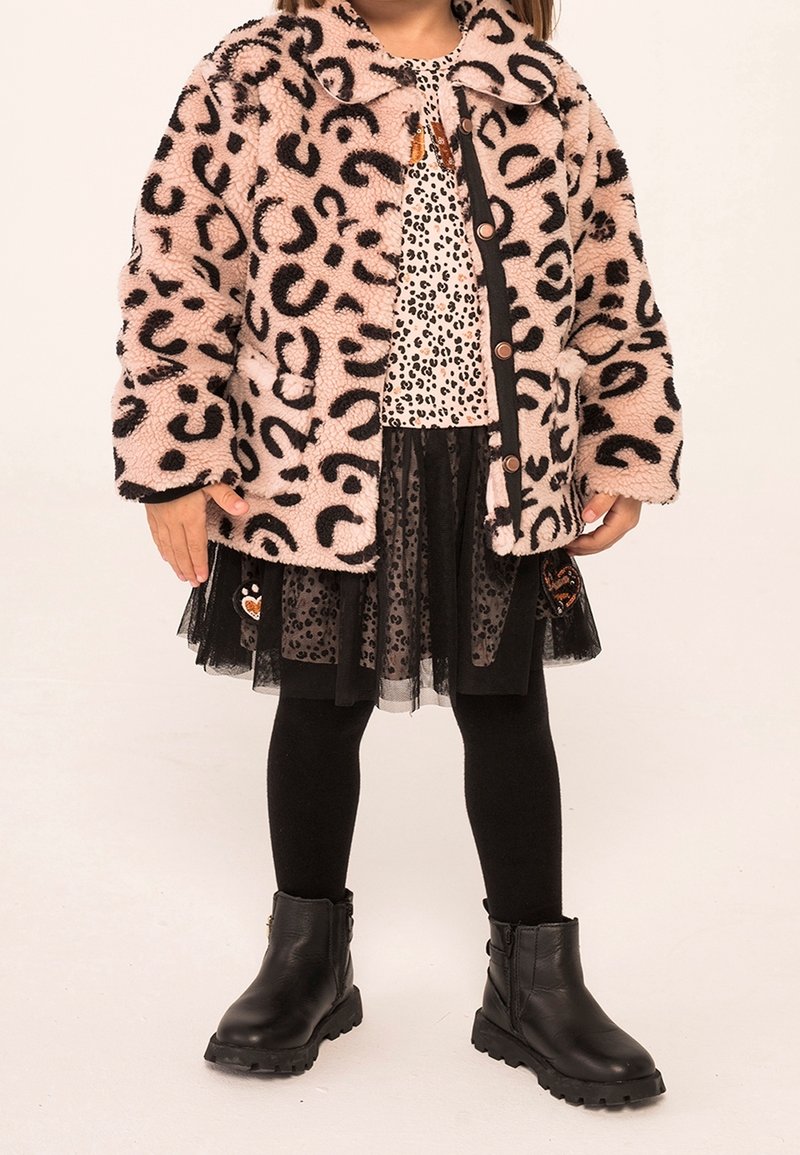 Rosa Leopardenmuster-Faux-Fur-Jacke, schwarzes und weißes gepunktetes Oberteil, schwarzer Tüllrock, schwarze Leggings und schwarze Ankle-Boots mit strukturierten Sohlen.