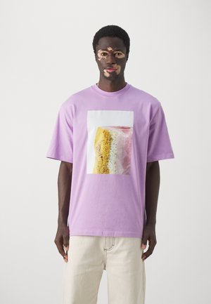 Purple cotton t-shirt featuring a large graphic of layered cake in yellow, pink, and beige tones on a white background. Casual fit.