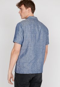 Camicetta a maniche corte in azzurro chiaro, realizzata in un tessuto testurizzato. Presenta un colletto e una vestibilità rilassata con un orlo dritto.