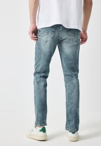 Jeans de mezclilla azul claro con corte recto, que cuentan con bolsillos traseros y un ligero desvanecimiento en la parte delantera. Llevados con zapatillas blancas con detalles en verde.