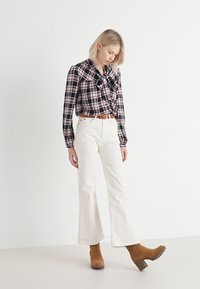 Camicia a quadri con colletto arricciato, con motivi blu, bianchi e rossi; abbinata a jeans bianchi a zampa d'elefante e stivaletti marroni.