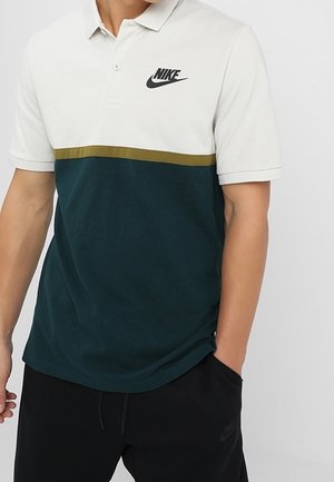Polo shirt featuring a white upper, green lower section, and a gold horizontal stripe. Includes a black Nike logo and soft texture.