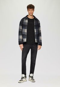 Kariertes Flanelljackett in Marineblau, Grau und Weiß, kombiniert mit einem schwarz-gemusterten T-Shirt, schwarzen Skinny-Jeans und zweifarbigen Sneakers.