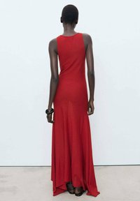 Abito maxi rosso senza maniche con gonna svasata. Tessuto morbido e leggero, con un orlo asimmetrico e design a schiena scoperta. Aspetto minimalista nel complesso.