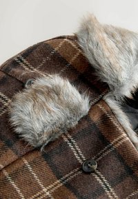 Pruun ruuduline mantel kunstnaha kraega, tumedate nööpidega ja pehme villase tekstuuriga. Kujundusel on silmatorkavad vertikaalsed ja horisontaalsed jooned.