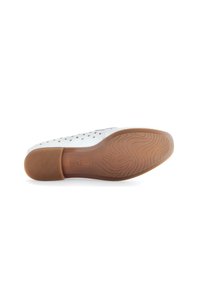 Witte geperforeerde schoen met een flexibele bruine rubberen zool. Opvallend logo op de zool en gestructureerd patroon over het onderste oppervlak.