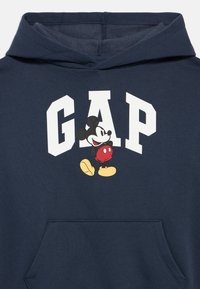 Granatowa bluza z kapturem z białym napisem „GAP” i grafiką Myszki Miki w czerwonych spodenkach i żółtych butach, przechodzącej przez litery.