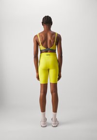 Felgekleurde gele sportkleding met een lage rugontwerp. De sportbeha heeft grijze bandjes met verstelbare sluitingen. De shorts zijn strak en van een gladde stof.