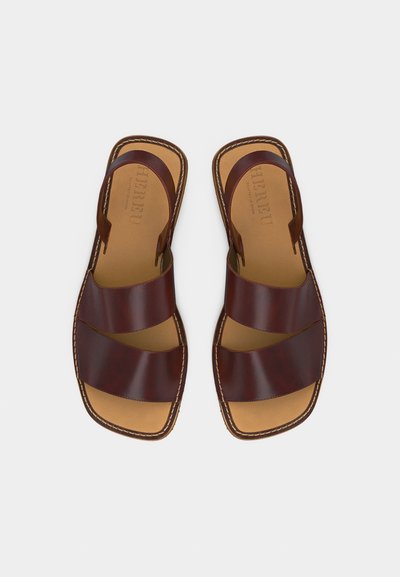 Ζευγάρι καφέ δερμάτινων σανδαλιών με δύο φαρδιές λουρίδες και ανοιχτή μύτη, τοποθετημένα δίπλα-δίπλα σε λευκό φόντο.