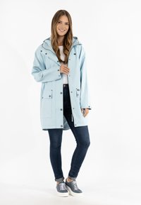 Ljusblå vattentät jacka med huva, tryckknappar och två främre fickor. Matchas med mörka jeans och grå sneakers.