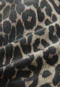 Tissu à imprimé léopard avec des motifs noirs et beige, présentant une surface texturée et des fibres visibles. Le matériau semble être du coton.