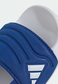 Sandalia con suela azul, parte superior texturizada, tres ranuras horizontales, detalles blancos y plantilla acolchada y lisa. Construcción robusta visible.