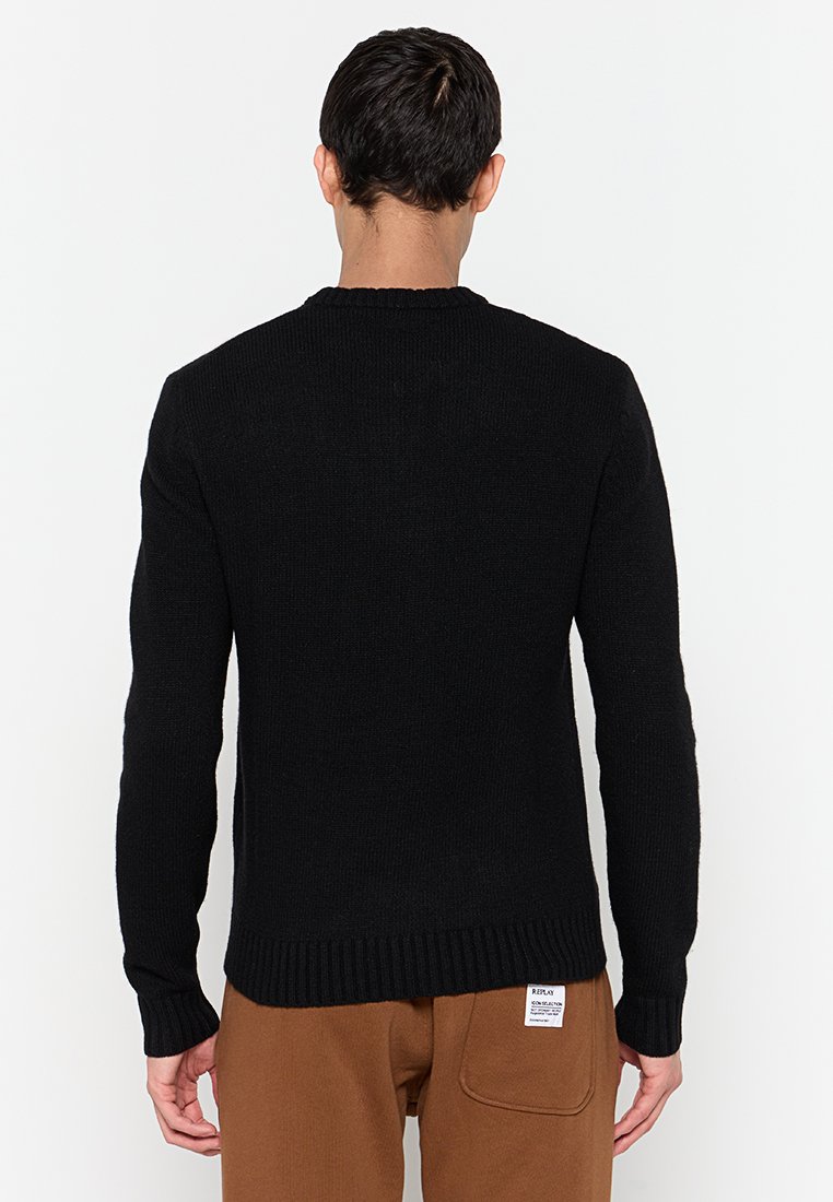 Schwarzer Strickpullover mit Rundhalsausschnitt, gerippten Bündchen und Saum, aus einem strukturierten Material. Das Model steht mit dem Rücken zur Kamera und zeigt das Rückendesign.