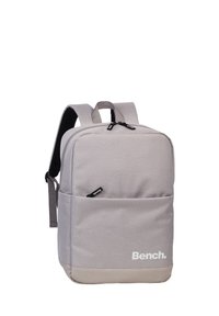 Grijze stoffen rugzak met een gladde textuur, rechthoekige vorm, ritssluitingen en een wit "Bench." logo op de voorkant.