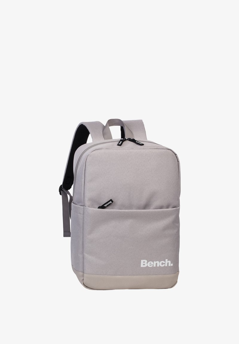 Grijze stoffen rugzak met een gladde textuur, rechthoekige vorm, ritssluitingen en een wit "Bench." logo op de voorkant.