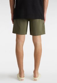 Shorts vert olive avec une texture lisse, arrivant au genou, et une ceinture élastique, accompagnés d'une paire de chaussures légères à enfiler.