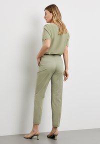Light green short-sleeve top with a relaxed fit, paired with matching fitted trousers, and minimalist green heels. Smooth texture, no visible patterns.