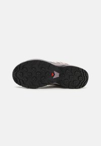 Semelle de chaussure avec des crampons en caoutchouc multidirectionnels ; noire avec des motifs circulaires et angulaires en relief ; accent central rouge contrastant.