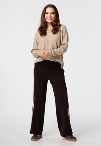 Pull en tricot côtelé beige associé à un pantalon large noir avec des rayures blanches sur les côtés. Le mannequin se tient contre un fond uni.